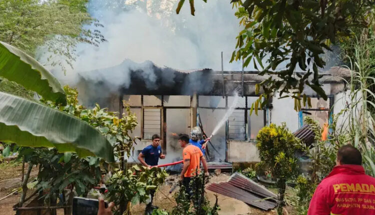 KEBAKARAN— Petugas Damkar melakukan penyemprotan air untuk memadamkan api yang membakar rumah
dinas guru di SDN 18 Nagari Pematang Panjang, Sijunjung.